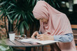 © palidachan - Muslim female student taking down note in diary. Concentrated girl studying on a book and taking down note sitting at the desk.
