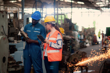 Caucasian woman programmer engineer and African Technician machine is working in factory and checking machinery operating In the midst of the sparks from machine repair to be dangerous.	