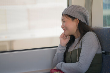 Poster - lifestyle portrait of young happy and beautiful Asian Chinese woman excited and cheerful looking through window sitting on train enjoying landscape from the railcar glass