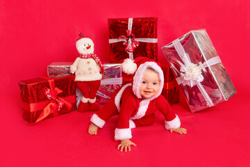 happy little baby six months old in Santa costume sitting near gifts on red isolated photophone, space for text, new year and holiday concept