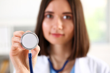 Wall Mural - Female medicine doctor hand holding stethoscope head closeup in front of her chest. Medic shop or store, physical and disease prevention, er consultant, 911, pulse measure, healthy lifestyle concept