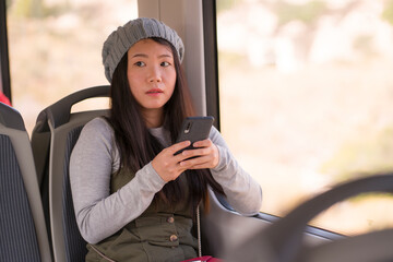 Canvas Print - lifestyle portrait of young beautiful and attractive Asian Korean woman in winter hat sitting by window on train using internet mobile phone in transportation concept