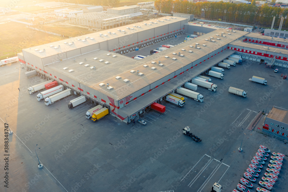 Logistics park with warehouse, loading hub and many semi trucks with cargo trailers standing at the ramps for load/unload goods at sunset.  - obrazy, fototapety, plakaty 