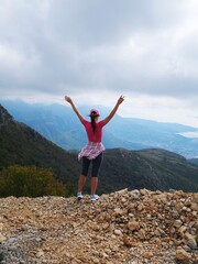 A girl in a sports T-shirt and gray leggings stands with her back and looks at the mountains with her hands up