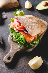 Wall Mural - Healthy sandwich with rye bread bun, salmon, avocado, onion and salad served on a wooden rustic board.