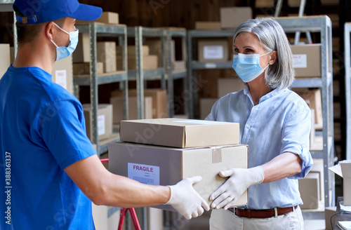 Cuadros en Lienzo Female manager supervisor wearing face mask preparing fast drop shipping safe delivery giving parcels packages boxes to male courier taking ecommerce orders to deliver standing in warehouse storage