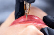 © Parilov - Applying red pigment with tattoo machine on woman lips, permanent makeup in beauty salon