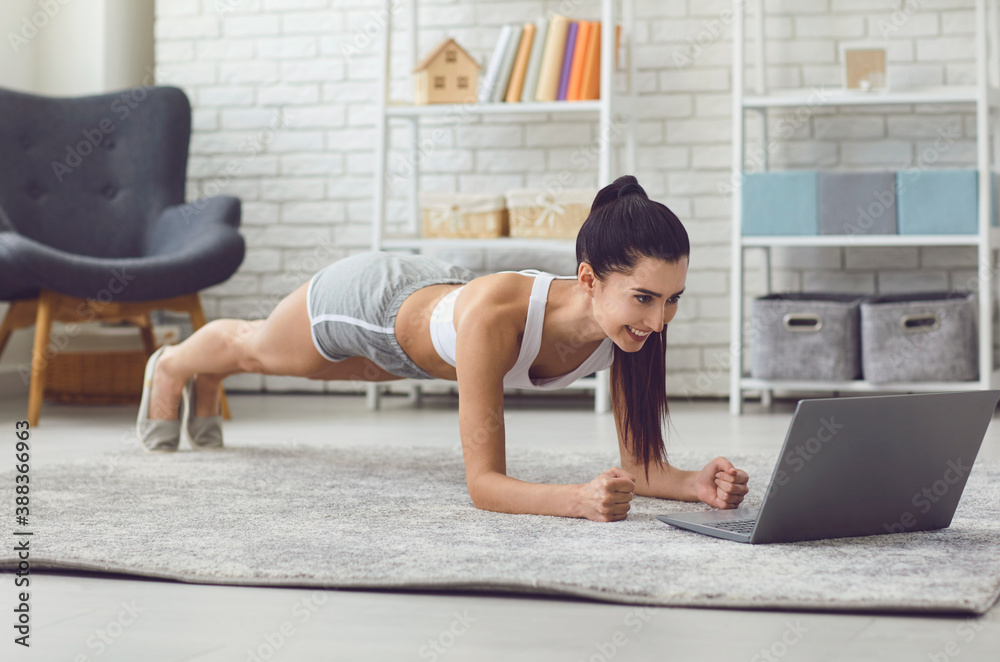 Smiling strong millennial girl making plank in front of laptop in living room online. - obrazy, fototapety, plakaty 