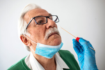 Female doctor specialist with face mask holding buccal cotton swab and test tube ready to collect DNA from the cells on the inside of a senior man patient