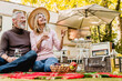 © InsideCreativeHouse - Aged beautiful caucasian couple having picnic and drinking champagne in the yard near the motorhome.Mature blond lady pointing at something