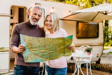 Wall Mural - Energetic elderly european couple looking at the map with their caravan home behind