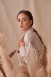 © Dmitry Tsvetkov - Tender soft studio portrait of elegant female model posing between ears of rye at textile background. Girl in brown skirt and beige jacket. Young woman with brunnette hair in pony tail