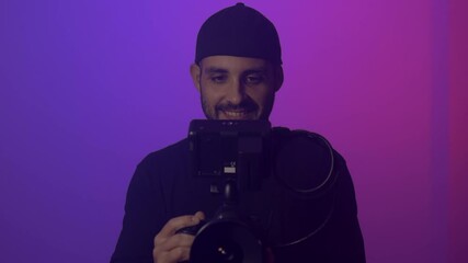 Wall Mural - Professional cameraman is recording on a set with cinema camera. Purple background. Broadcasting, video making  and cinematography concept