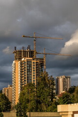 Wall Mural - Construction of new high-rise buildings in Coquitlam City, industrial construction site, construction equipment, two construction cranes on the background of stormy cloudy sky