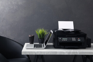 New modern printer, laptop and cup of drink on grey table indoors