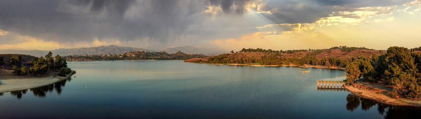 a breathtaking aerial panoramic shot of the still blue waters and lush green trees and majestic mountain ranges at Frank G Bonelli Regional Park at Puddingstone Lake in San Dimas California