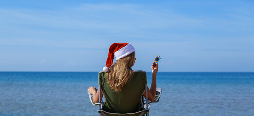 travel on New year's eve on beach by sea. girl in Christmas hat is sunbathing in sun. woma,n with dark glasses. woman in chair with her back to camera looks into distance. Tourist resting by water.