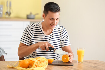 Canvas Print - Handsome man cutting ripe oranges in kitchen