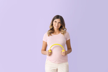 Wall Mural - Beautiful pregnant woman putting headphones on her belly against color background