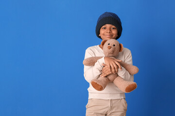 Poster - Cute African-American boy in winter clothes and with toy on color background