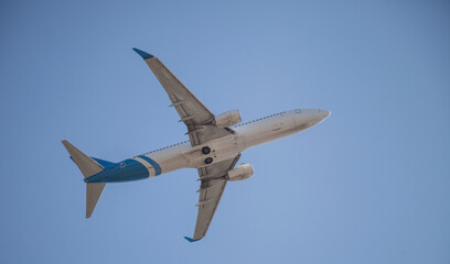 White plane flies in the sky. Bottom view. Takeoff and landing. Arrival and departure. Passenger plane isolated on blue background. Passenger airplane. Travel by air transport. Copy space. Flying.