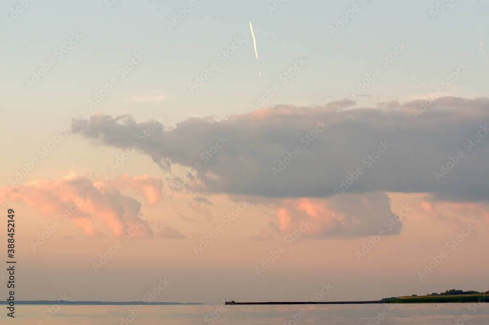 Krajobraz molo i widok nieba podświetlonego zachodzącym słońcem z chmurami i śladem na niebie po przelatującym samolocie - obrazy, fototapety, plakaty 