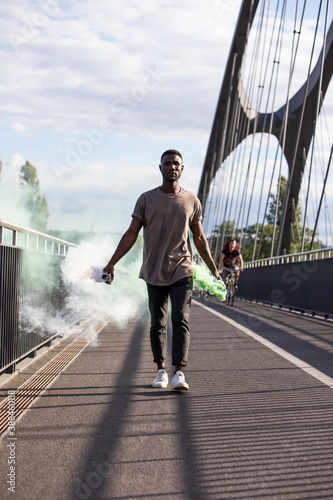 Young Black Man Walking with Green Smoke Bombs in Hands