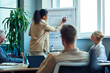 © Kostiantyn - Discussing business strategy. Young mixed race business woman drawing a graph on flipchart, giving a presentation to colleagues while having a meeting in the modern office