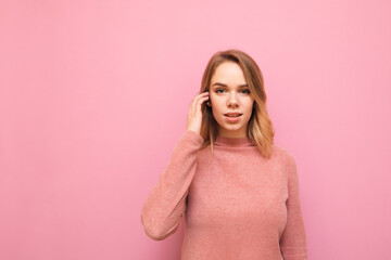 Attractive blonde girl with serious face posing at camera on pink background, closeup portrait. Serious pretty lady in sweater isolated on pink, looking into camera. Copy space