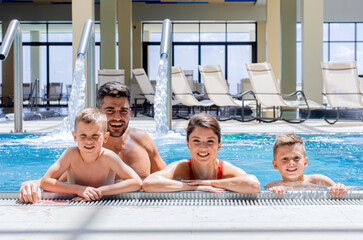 Wall Mural - smiling family of four having fun and relaxing in indoor swimming pool at hotel resort.