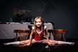 A little girl in a red-and-white gymnast's outfit sits on a twine on chairs in a dark room. Girl gymnast demonstrates the twine. Sports concept.