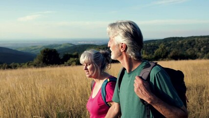 Wall Mural - Active senior couple hiking in nature with backpacks, enjoying their adventure at sunset.