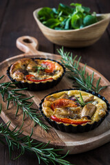 Wall Mural - Two vegetarian tartlets on a wooden board and a wooden bowl with fresh field salad on a rustic table, vertical stock photo