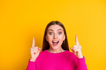 Wall Mural - Photo of pretty girl direct fingers look up empty space amazed open mouth wear pink sweater isolated yellow color background