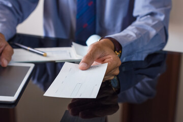 Wall Mural - Business man or manager in suit hand  giving bank check to colleague with checkbook on the desk at office. Payday and payment by cheque concept