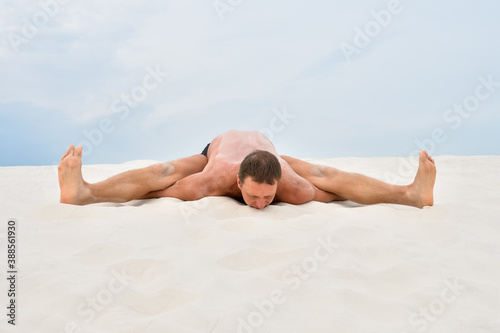 Young man in yoga pose kurmasana on the beach