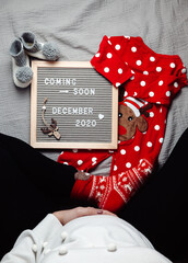 Pregnant woman sitting with a coming soon December 2020 Baby announcement sign. Coming soon Christmas concept. Pregnancy belly. 
