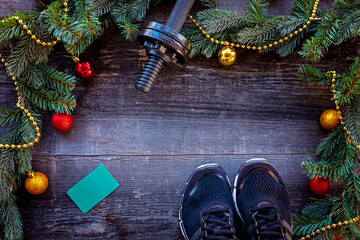 Christmas and Happy new year background with dumbbells, yoga mat, sneakers, branches fir tree glass balls and bows bells on white background. Copy space. Flat lay, top view.