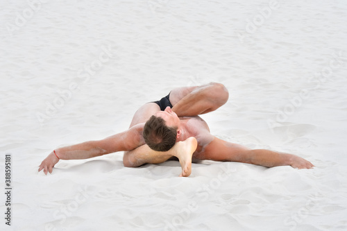 Young man in yoga pose on the sand at the beach