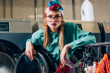 Sticker - woman in glasses and turban holding magazine near modern washing machine in public laundromat