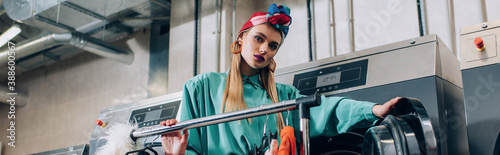 Cuadros en Lienzo young and stylish woman in turban standing near washing machines in modern laund