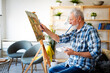 © NDABCREATIVITY - Smiling mature man painting on canvas at home