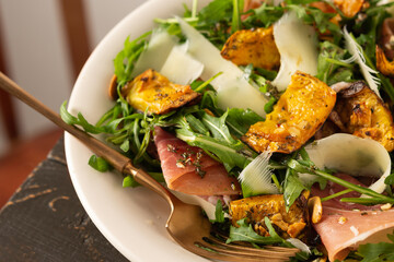 Light autumn salad with arugula, baked pumpkin, prosciutto and young parmesan, a plate of salad on a wooden table