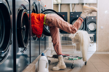 Sticker - young woman checking inside of washing machine near detergent bottle and cart with dirty clothing