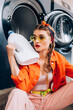 young woman in sunglasses holding bottle with detergent in laundromat