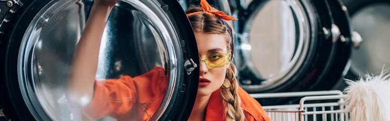 Sticker - young woman in sunglasses looking at camera through door of washing machine, banner