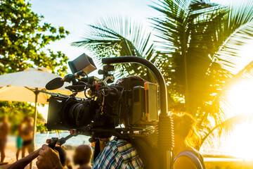 Beach video making, prefessional videographer taking video of young people at summer beach party. sunny tropical day. sun rays beam