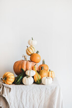 Colorful Pumpkins Of Different Shapes And Size In Pyramid Composition On Light Tablecloth, White Wall At Background. Pumpkins For Halloween Or Thanksgiving Day Autumn Holiday Decoration Concept
