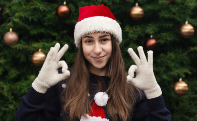 Everything will be fine for christmas. Close up Portrait of woman wearing a santa claus hat with emotion. Against the background of a Christmas tree