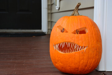 A jack-o-lantern with toothpicks for teeth sit on the front porch of a home during Halloween.